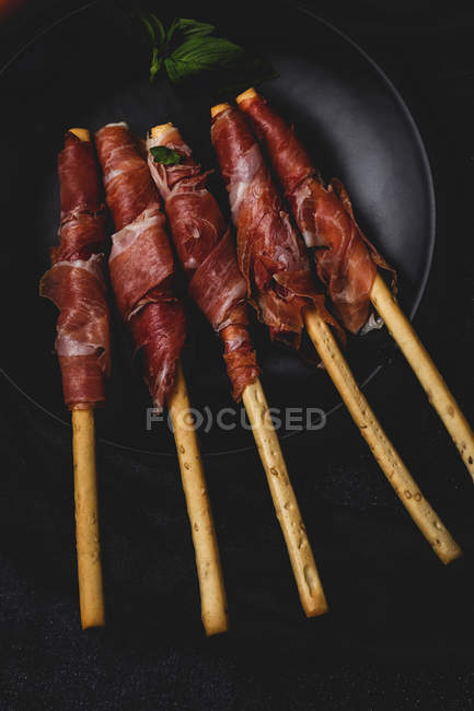 Gressini con tipico prosciutto serrano spagnolo su piatto su fondo nero — Foto stock