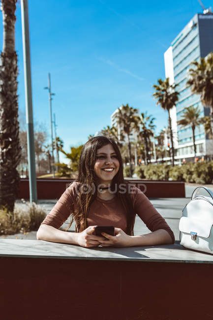 Девочка-подросток смотрит на свой смартфон на улице в солнечный день — стоковое фото