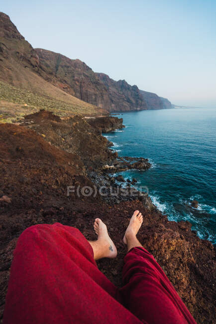 Pernas de cultivo de humanos que se encontram na costa rochosa perto do mar e da montanha Teide em Tenerife, Ilhas Canárias, Espanha — Fotografia de Stock