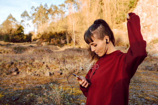 Jovem hipster mulher com a mão levantada ouvir música com telefone celular e dançar no campo — Fotografia de Stock