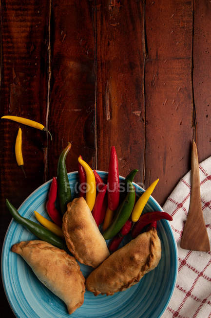 Conjunto de rissóis caseiros e pimentas verdes e vermelhas frescas na placa azul na mesa de madeira — Fotografia de Stock