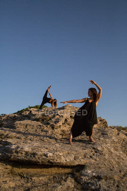Молодые загадочные балерины в черном танцуют на камнях в солнечный день — стоковое фото