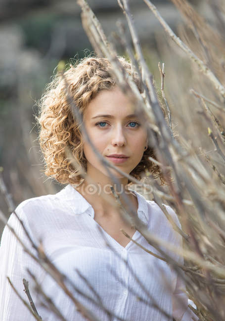 Young charming woman looking at camera near dry branches of shrub on blurred background — Stock Photo