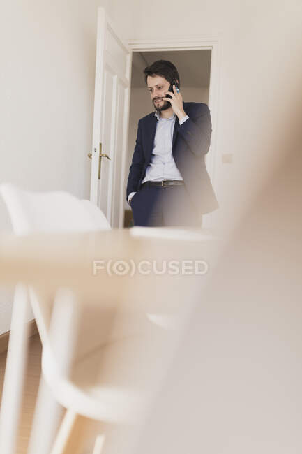 Concentrated young male with hand in pocket talking on mobile phone in room with chairs and table — Stock Photo