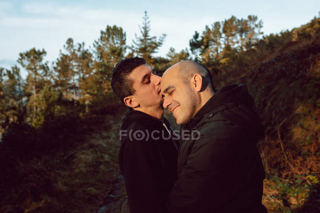 Feliz casal homossexual abraçando na floresta em dia ensolarado — Fotografia de Stock