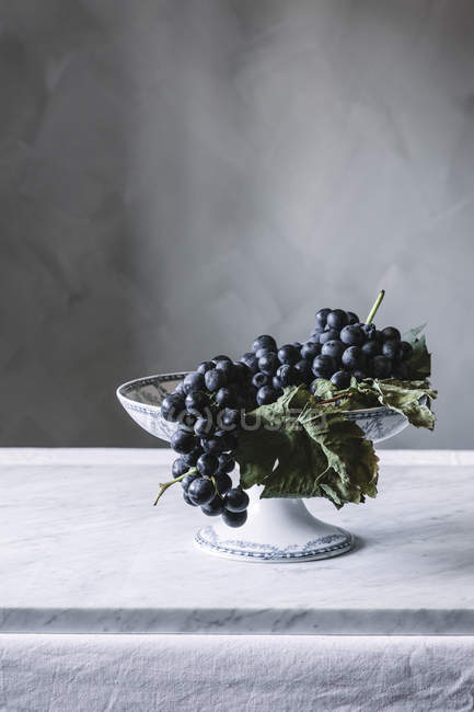 Grappolo d'uva fresca su piatto d'annata in tavola — Foto stock