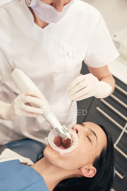 Mãos de dentista em luvas usando equipamento moderno para fazer a varredura de dentes de paciente feminino em consultório odontológico — Fotografia de Stock