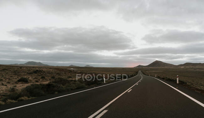 Живописный вид серого облачного неба над асфальтовой дорогой в великолепной сельской местности — стоковое фото