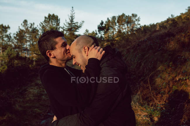 Feliz casal homossexual abraçando no caminho na floresta em dia ensolarado — Fotografia de Stock