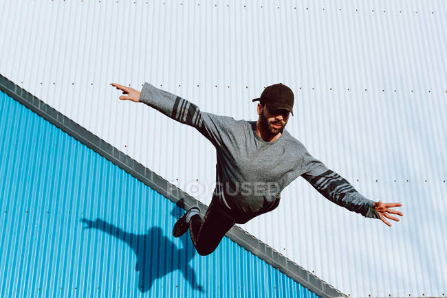 Guy in stylish outfit performing flip near wall of modern building on city street — Stock Photo