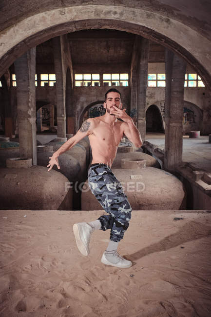 Shirtless man dancing on sand in old shabby building — Stock Photo