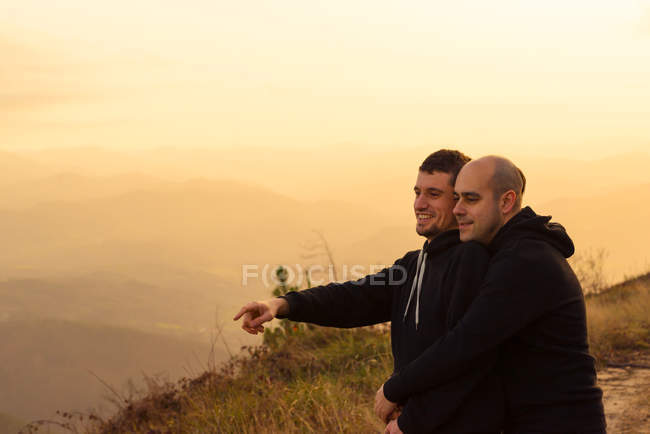 Romântico casal homossexual abraçando na rota em montanhas ao pôr do sol — Fotografia de Stock