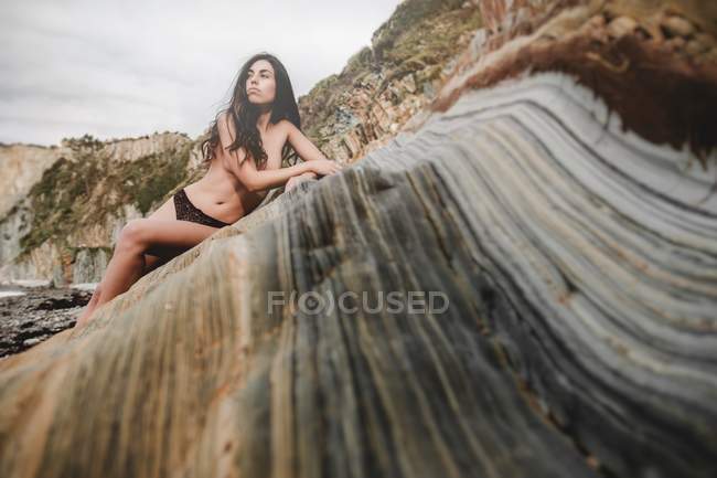 Nude brunette lady relaxing on rock on sea coast — Stock Photo