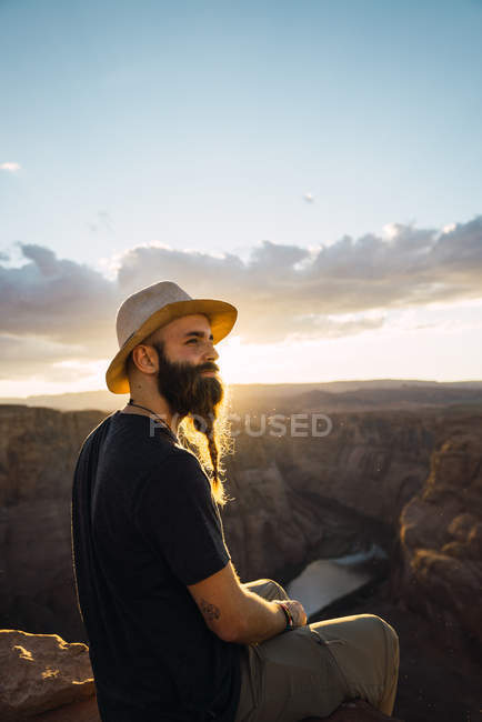 На виду бородатого чоловіка з рюкзаком, який дивиться на прекрасний каньйон і спокійну річку в сонячний день на західному узбережжі Уса — стокове фото