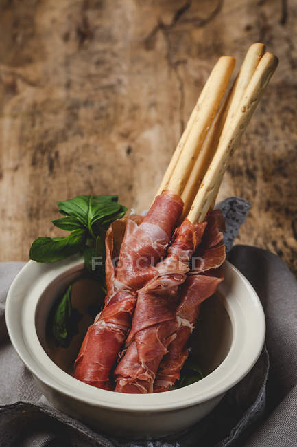 Gressini con tipico prosciutto serrano spagnolo in vaso sul tavolo di legno — Foto stock