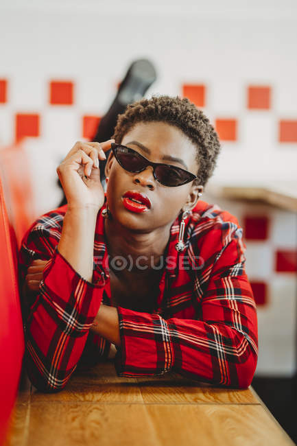 Confident African American woman lying on seats in cafe and looking at camera — Stock Photo