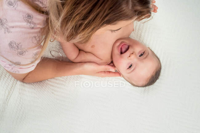 Зверху мама грає зі смішним маленьким голим новонародженим лежить на ліжку в кімнаті — стокове фото
