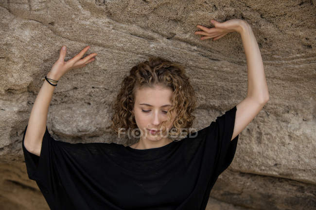 Jeune femme blonde avec les mains levées regardant vers le bas sous le rocher — Photo de stock
