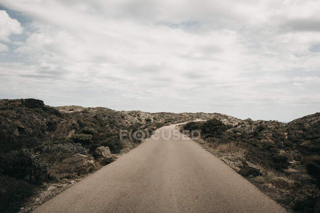 Beaux nuages blancs flottant sur un ciel bleu sur une colline rugueuse avec une route de campagne étroite — Photo de stock