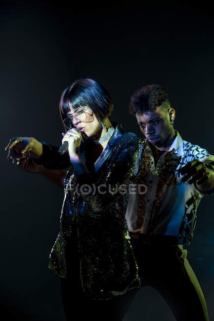 Bonito preto masculino dançando perto cantando feminino durante a performance no palco escuro — Fotografia de Stock