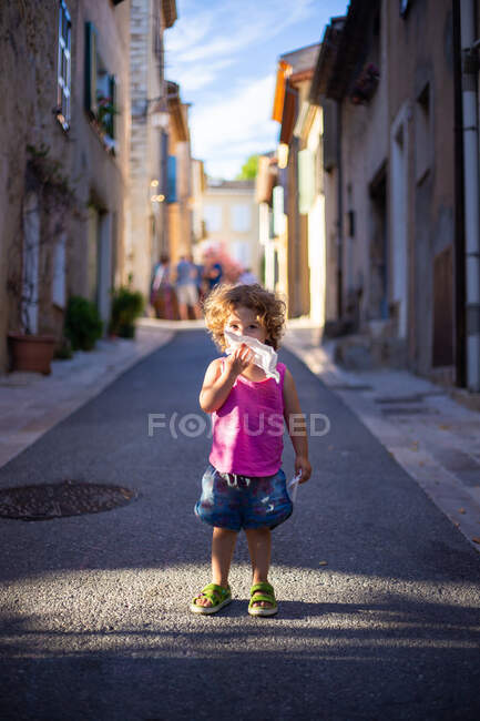 Happy funny girl cleaning mouth with napkin while standing on asphalt street between buildings in summer — Stock Photo