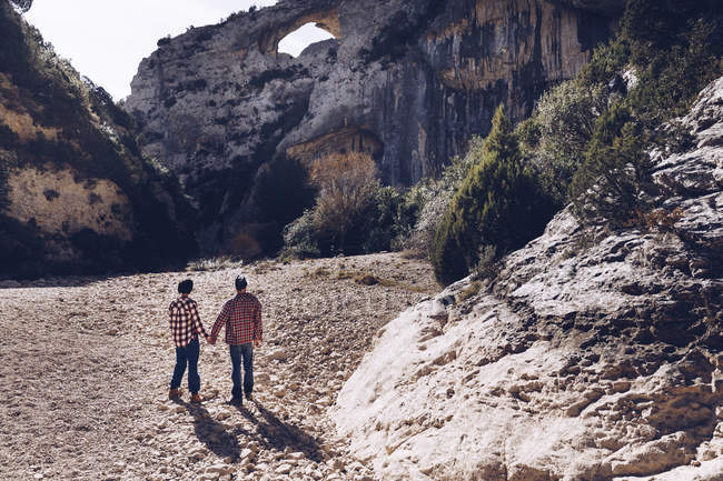 Молода пара тримає руки в каньйоні між скелястими горами в сонячний день — стокове фото