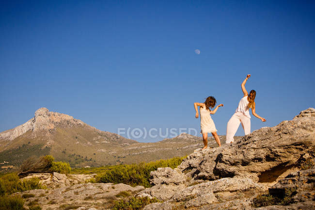Молоді таємничі жінки з посиленими руками позують на каменях біля пагорба і блакитного неба з місяцем — стокове фото