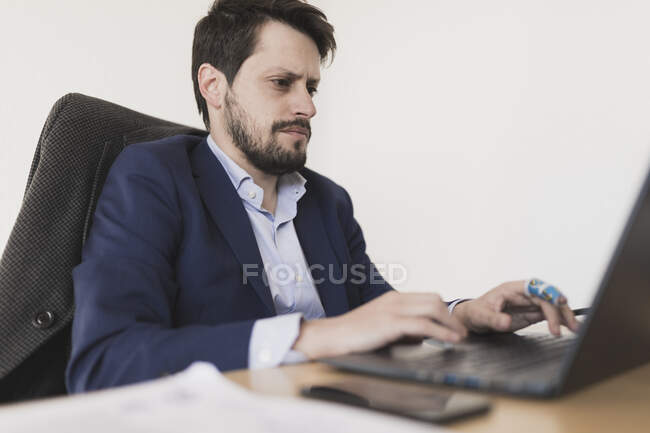 Концентрированный молодой мужчина просматривает ноутбук за столом в офисе — стоковое фото