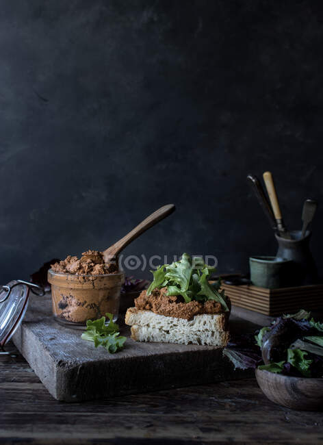 Sanduíche de patê de tomates secos, salada fresca e repolho na bandeja perto de faca na tábua de madeira no fundo preto — Fotografia de Stock
