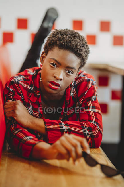 Selbstbewusste afrikanisch-amerikanische Frau liegt auf Sitzen im Café und blickt in die Kamera — Stockfoto
