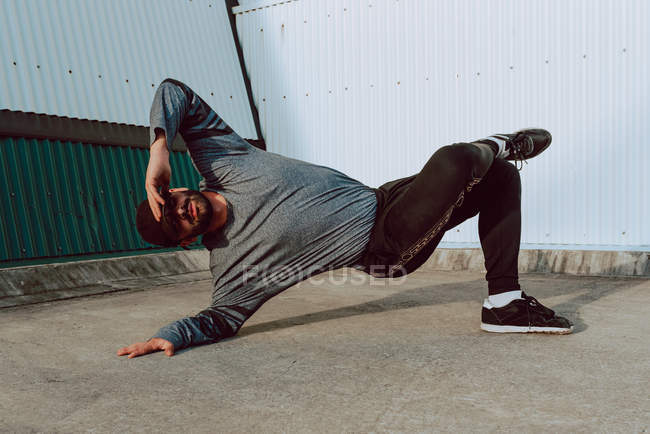 Stylish guy performing handstand and while dancing near wall of modern building on city street — Stock Photo
