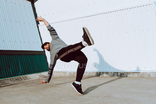 Guy in stylish outfit performing flip near wall of modern building on city street — Stock Photo
