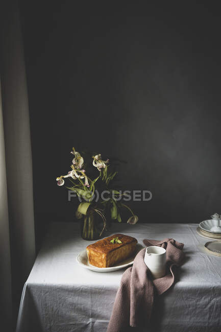Gâteau au citron et pichet servi sur une table rustique avec des fleurs — Photo de stock