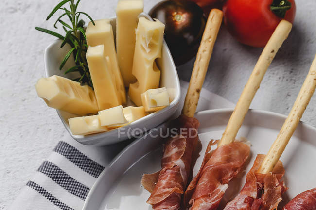 Gressini con tipico prosciutto serrano spagnolo su piatto bianco con formaggio in ciotola — Foto stock