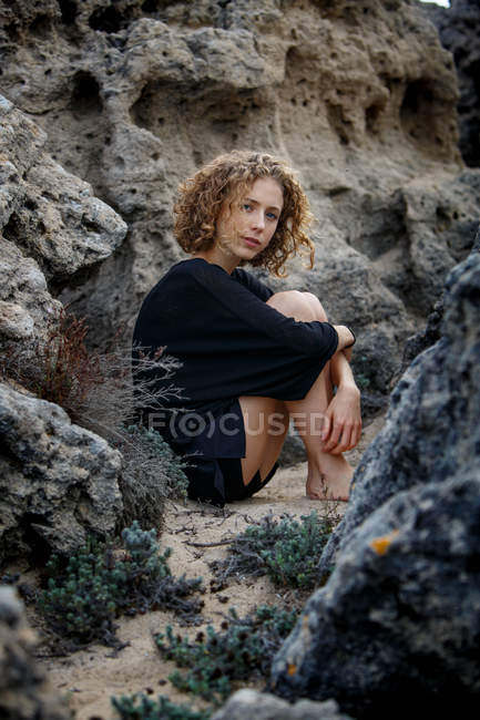 Junge nachdenkliche Frau sitzt in Steinen und umarmt Knie — Stockfoto