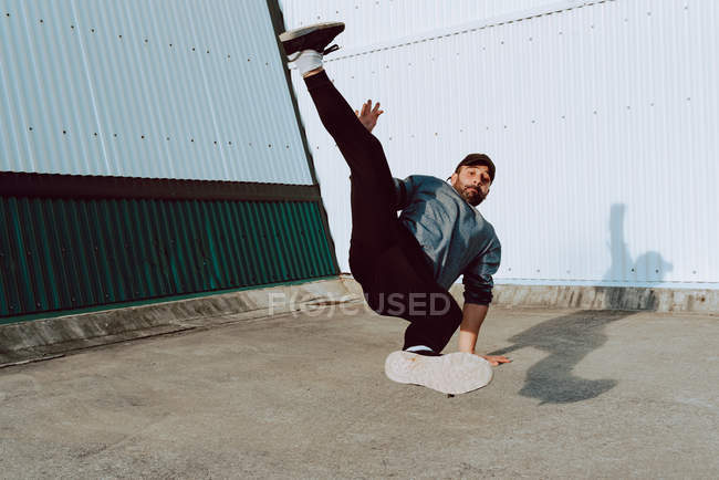 Guy performing handstand and looking at camera while dancing near wall of modern building on city street — Stock Photo