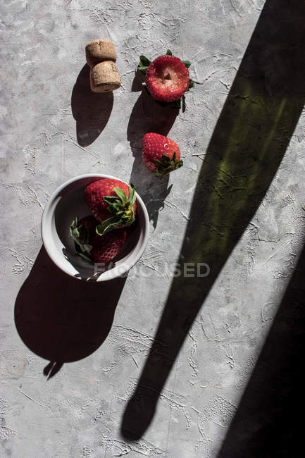 Fresh strawberries in bowl and on grey surface — Stock Photo