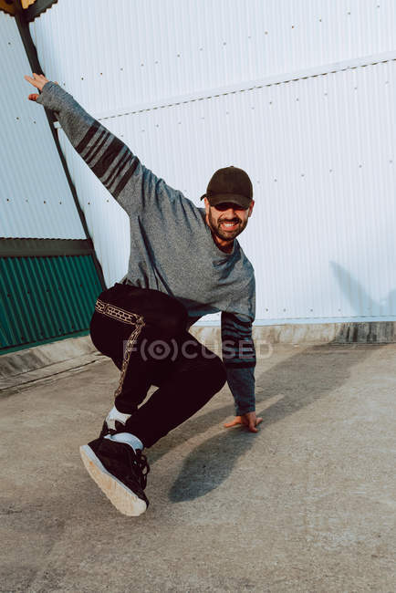 Улыбающийся парень танцует у стены современного здания на городской улице — стоковое фото