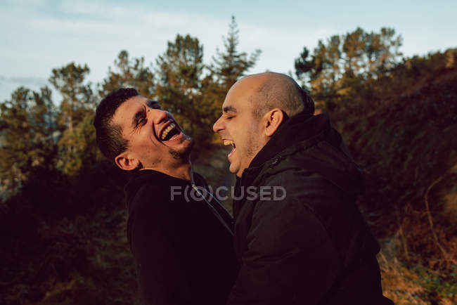 Ridere coppia omosessuale abbracciando sul sentiero nella foresta nella giornata di sole — Foto stock