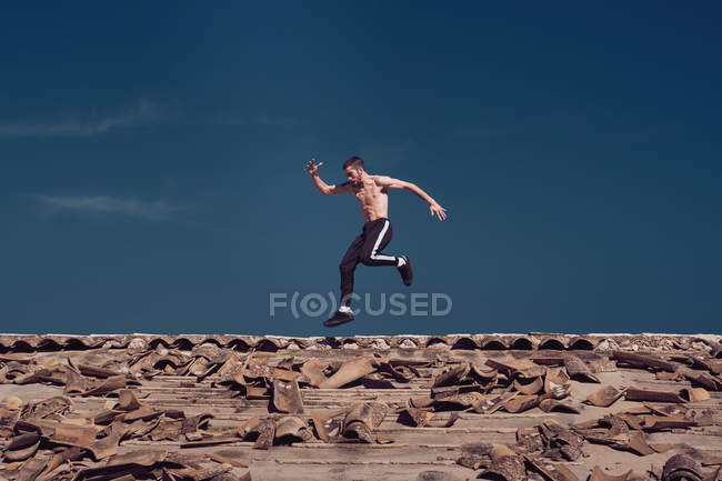 Man jumping while breakdancing on roof against blue sky — Stock Photo