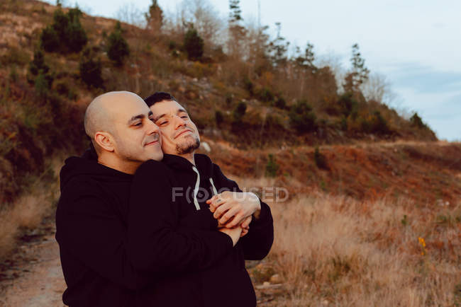 Romántico homosexual pareja abrazando en ruta en la naturaleza - foto de stock
