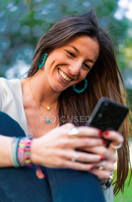 Retrato de jovem mulher usando smartphone sentado na grama no par — Fotografia de Stock