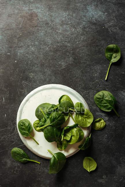 Folhas de espinafre frescas na placa branca na superfície cinzenta — Fotografia de Stock