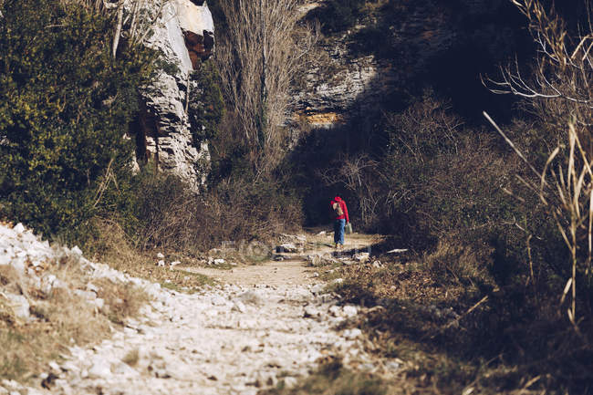 Жінка з рюкзаком і футляр, що йде по скелястій дорозі у величні дикі скелі — стокове фото