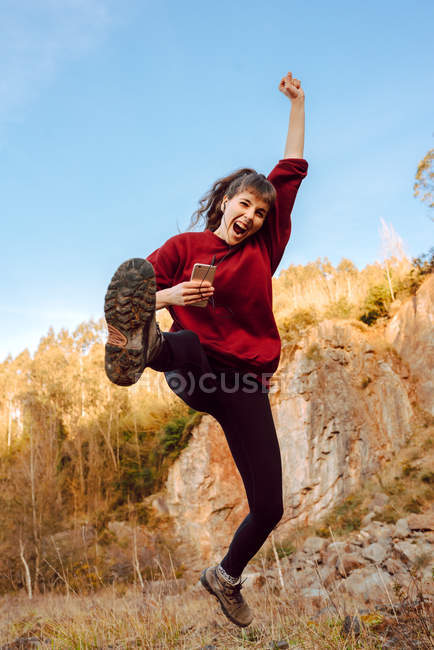 Junge Hipsterfrau mit erhobener Hand, die Musik auf dem Handy hört und in der Natur tanzt — Stockfoto