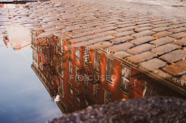 Riflessione di edificio rosso vecchio in acqua di pozzanghera su pavimentazione di ciottoli di strada, Nuova York — Foto stock