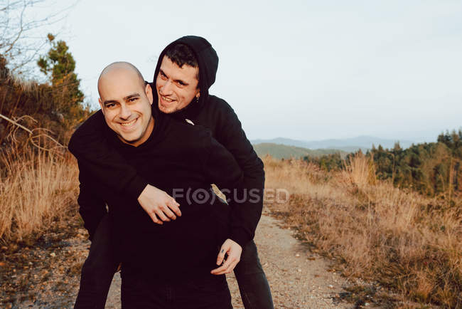 Happy homosexual couple having fun on route between plants in mountains — Stock Photo