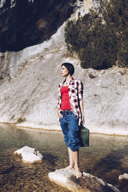 Mulher de pé na rocha com caso perto de água limpa no lago — Fotografia de Stock