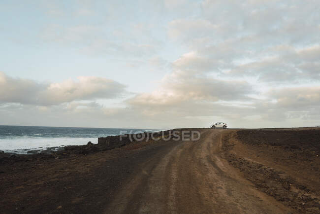 Voiture blanche moderne garée sur la route de campagne près de la mer ondulante par une journée nuageuse incroyable — Photo de stock