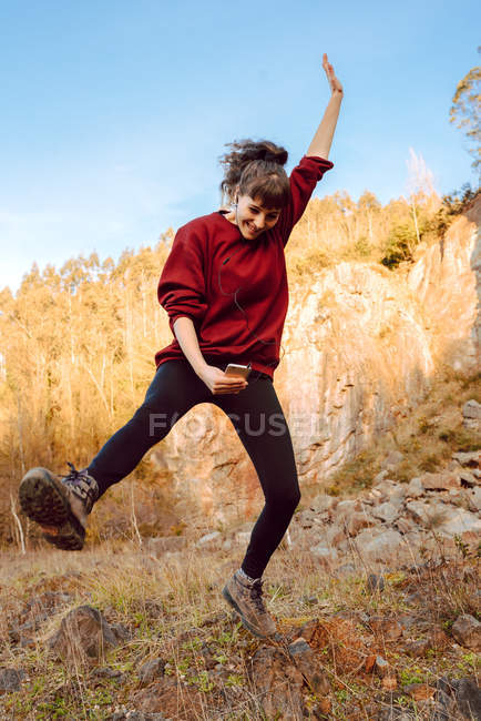 Young hipster woman with upped hand listening music on mobile phone and dancing in nature — Stock Photo
